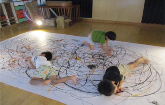 紙の上に寝転がって、自分を表現することに夢中な子供たちの写真